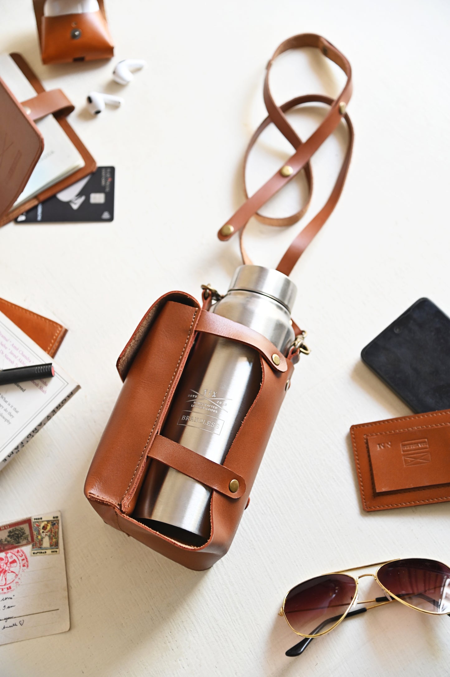 Brown handcrafted leather bottle case with utility pocket and steel flask, worn crossbody