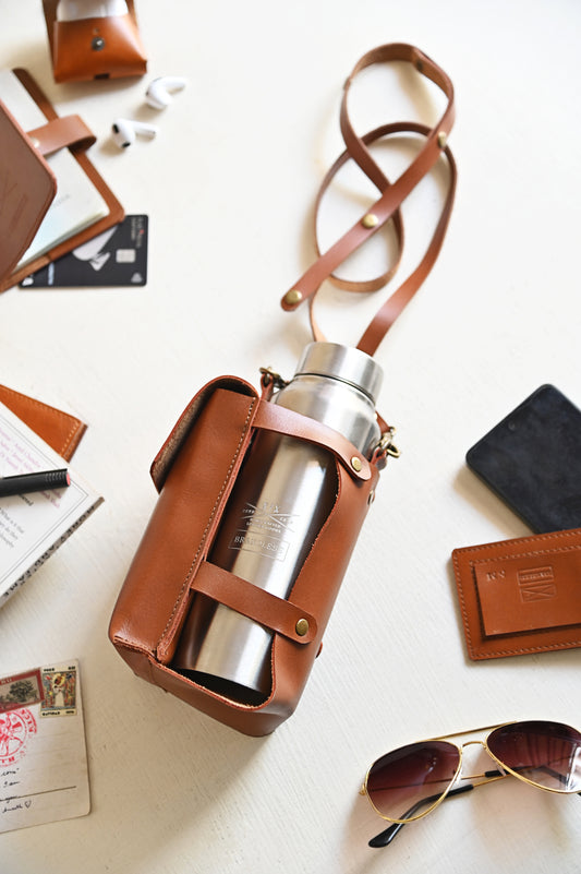 Brown handcrafted leather bottle case with utility pocket and steel flask, worn crossbody