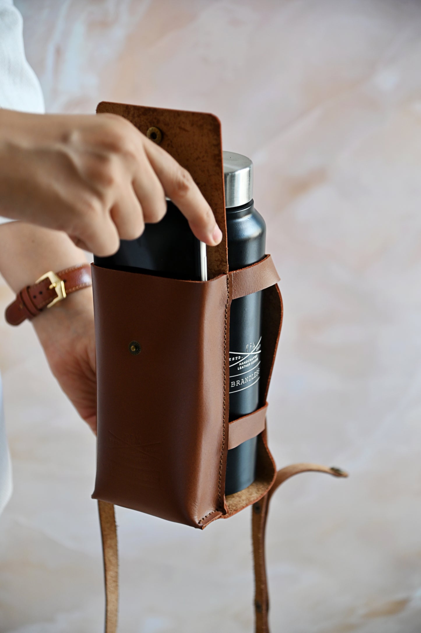 Brown handcrafted leather bottle case with utility pocket and steel flask, worn crossbody