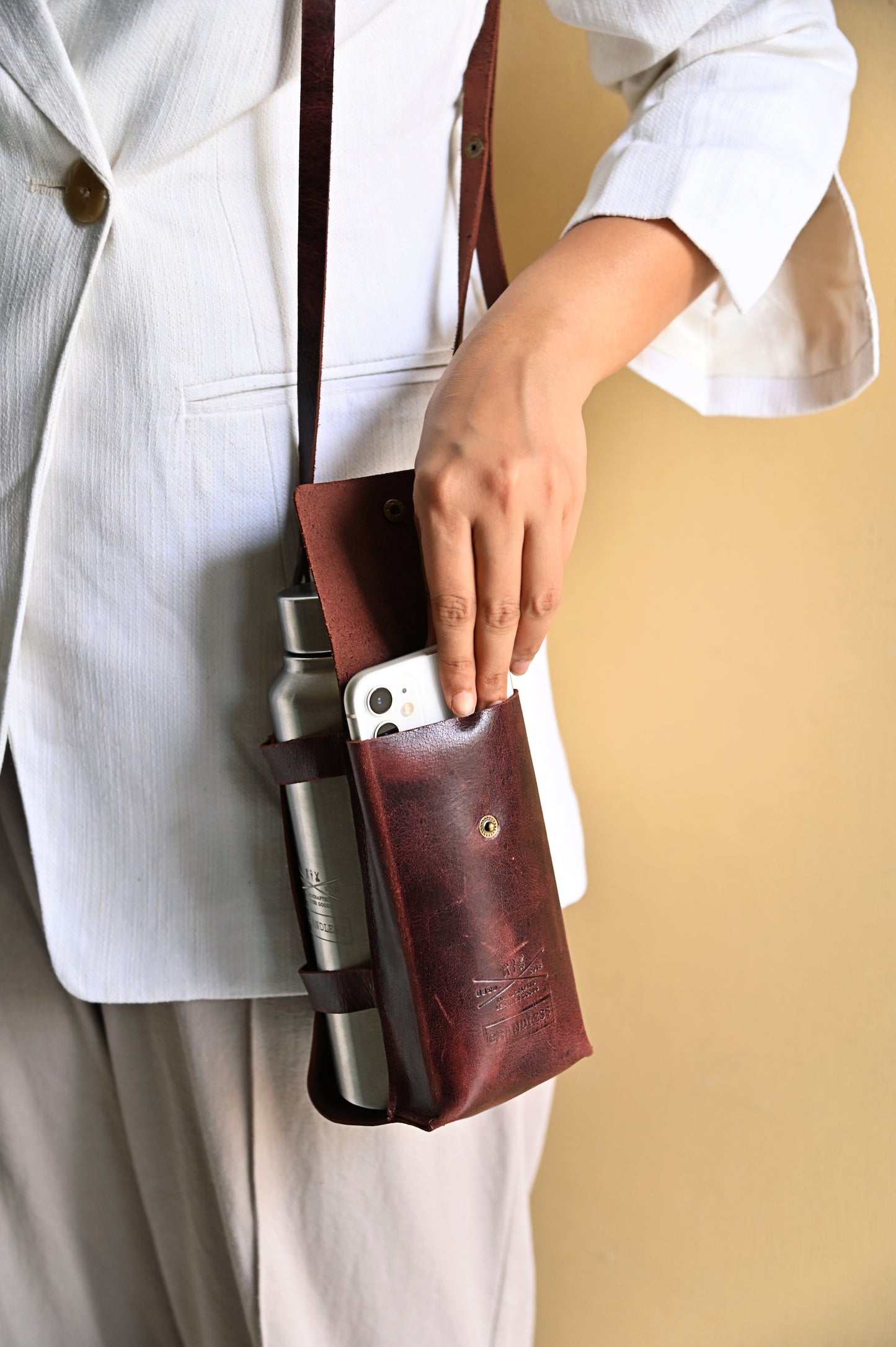Burgundy handcrafted leather bottle case with utility pocket and steel flask, worn crossbody