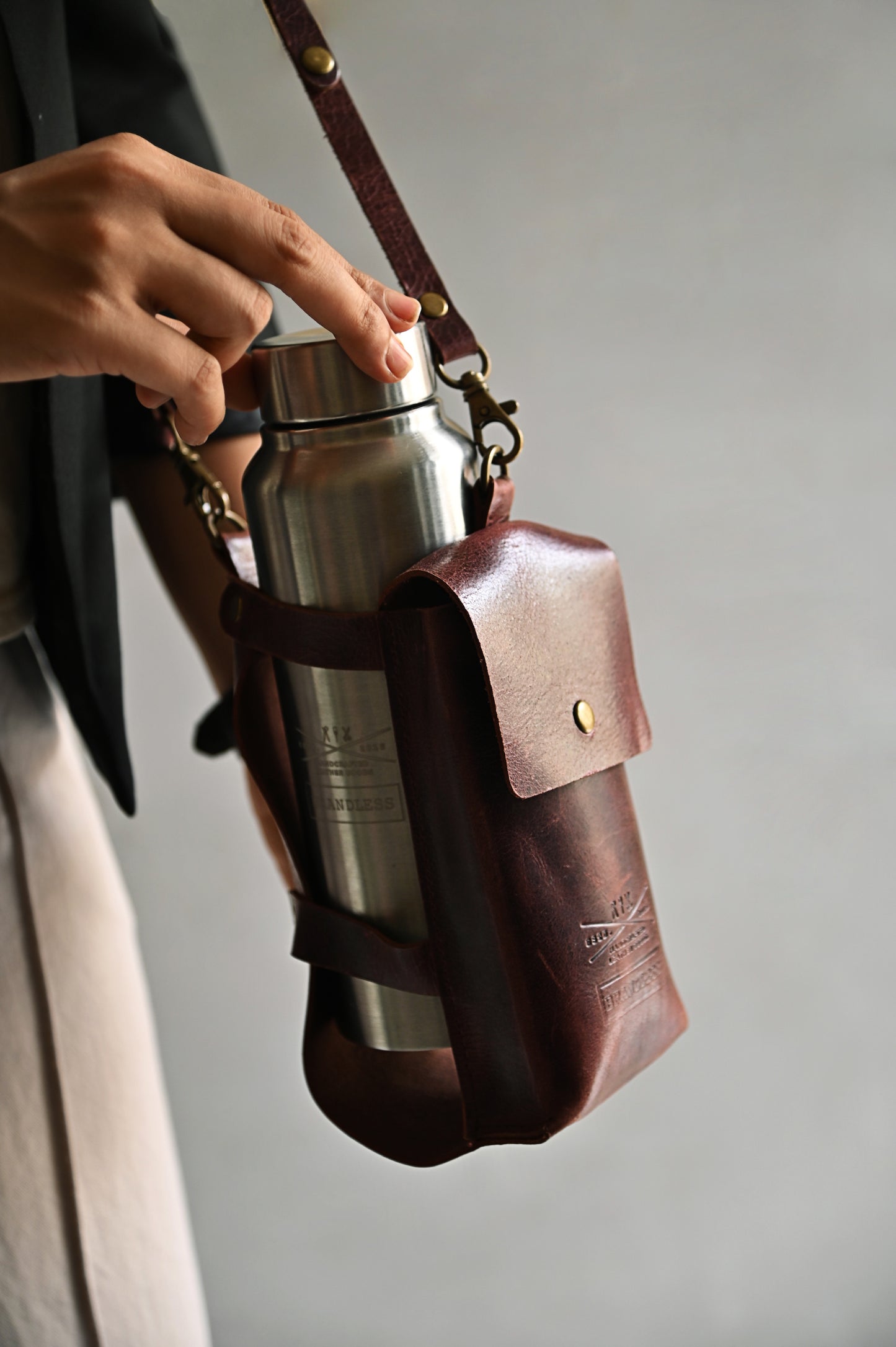 Burgundy handcrafted leather bottle case with utility pocket and steel flask, worn crossbody