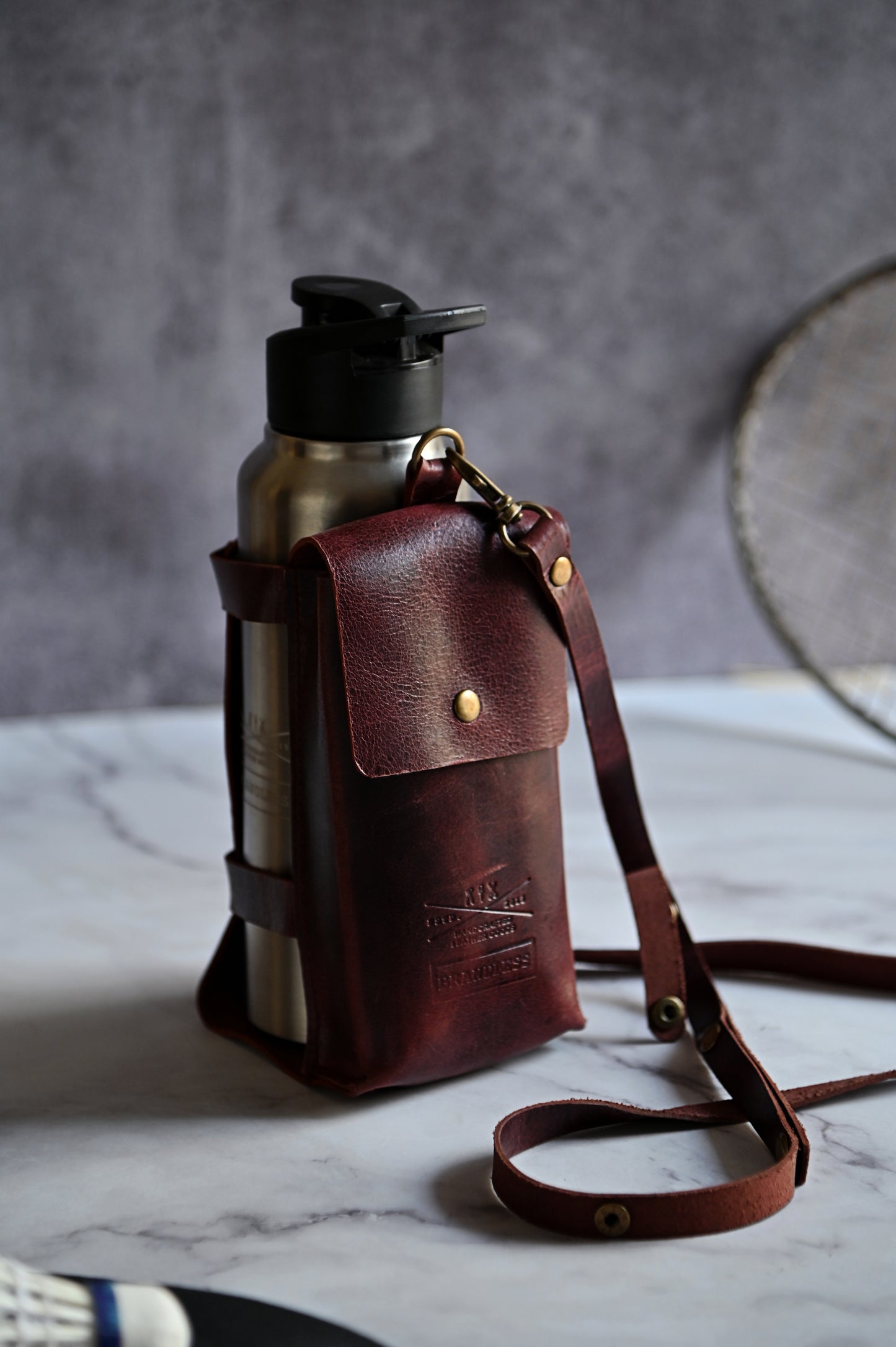 Burgundy handcrafted leather bottle case with utility pocket and steel flask, worn crossbody