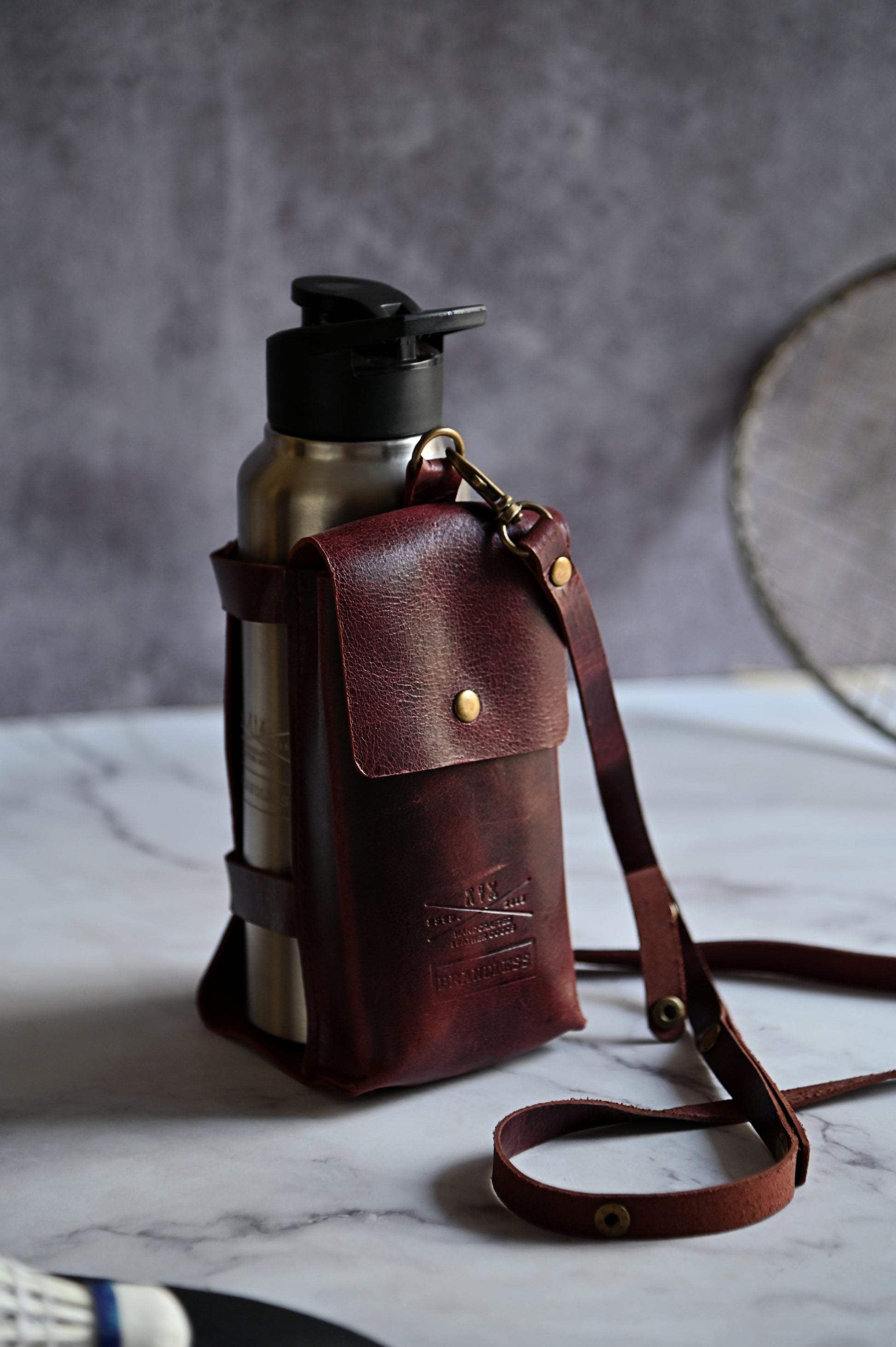 Burgundy handcrafted leather bottle case with utility pocket and steel flask, worn crossbody
